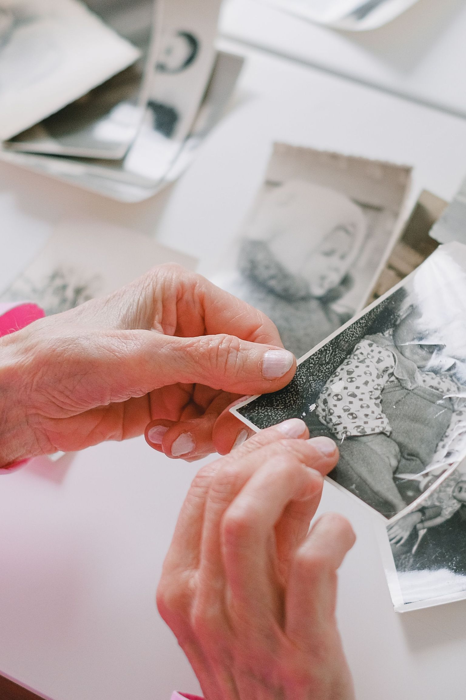 An elderly person with pink sleeves is reviewing nostalgic black and white photographs at a table.